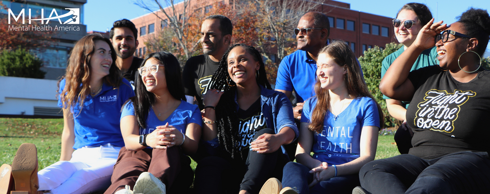 Diverse group of people ranging in age, race, and ethnicity sitting on grass smiling in the sunlight. 
